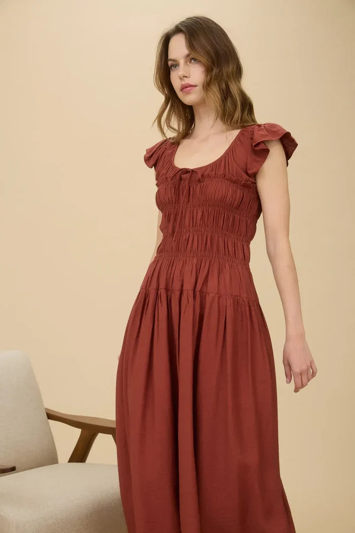 Rust-colored maxi dress with shirred bodice, ruffle sleeves, and tie neckline