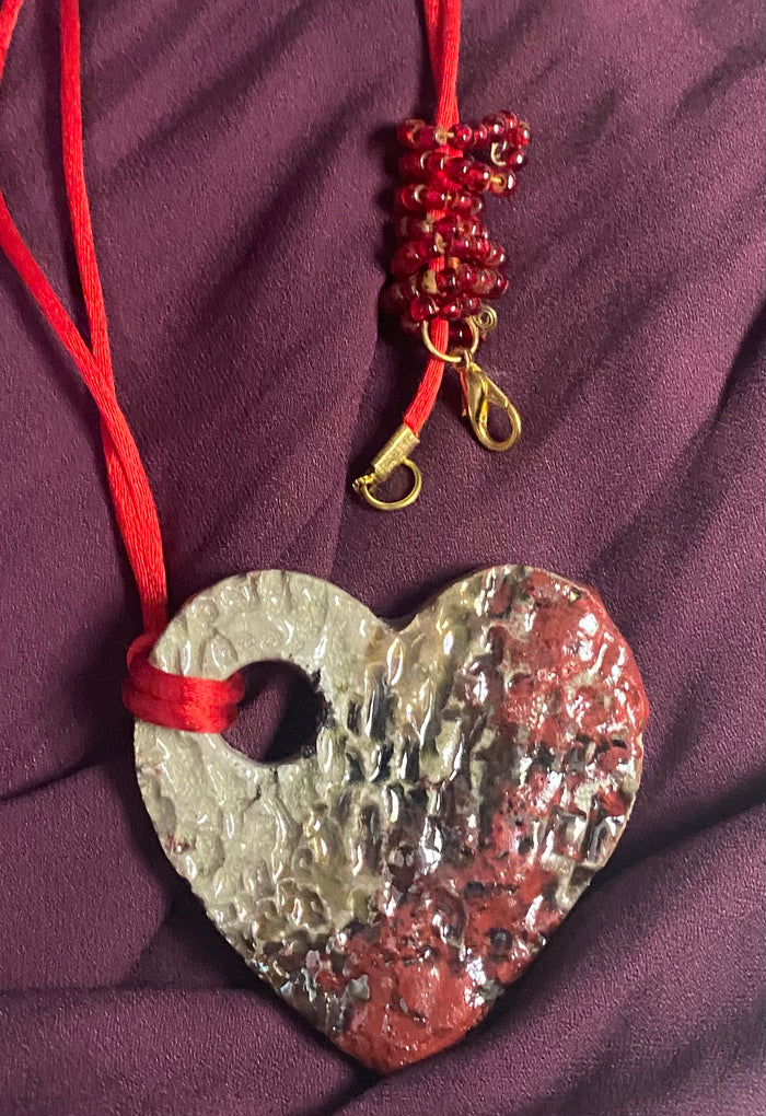 Have A Heart ! Each heart pendant is handmade with love! It is 3"x 3" and weighs approx. 3ozs. This pendant has a copper gold metallic raku glazes that renders a unique translucent  patina. The heart has a textured pattern . It holds a spiral of red mini beads on a spiral copper wire. This pendant has a nice 12" red suede cord!