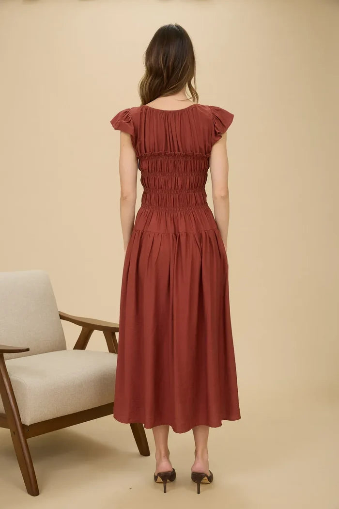 Woman modeling rust-colored midi dress with shirred bodice and ruffle sleeve detail