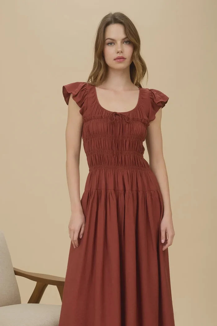 Woman modeling rust-colored shirred bodice ruffle midi dress with ruffled cap sleeves