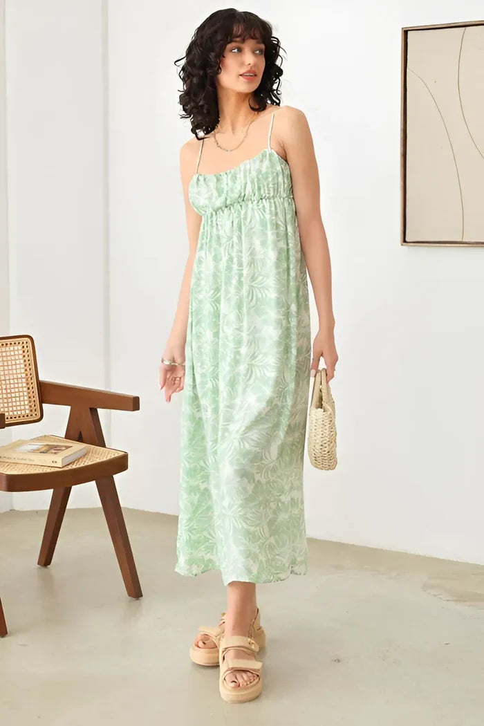 Woman in a green sleeveless shirring tropical print maxi dress in an empty room